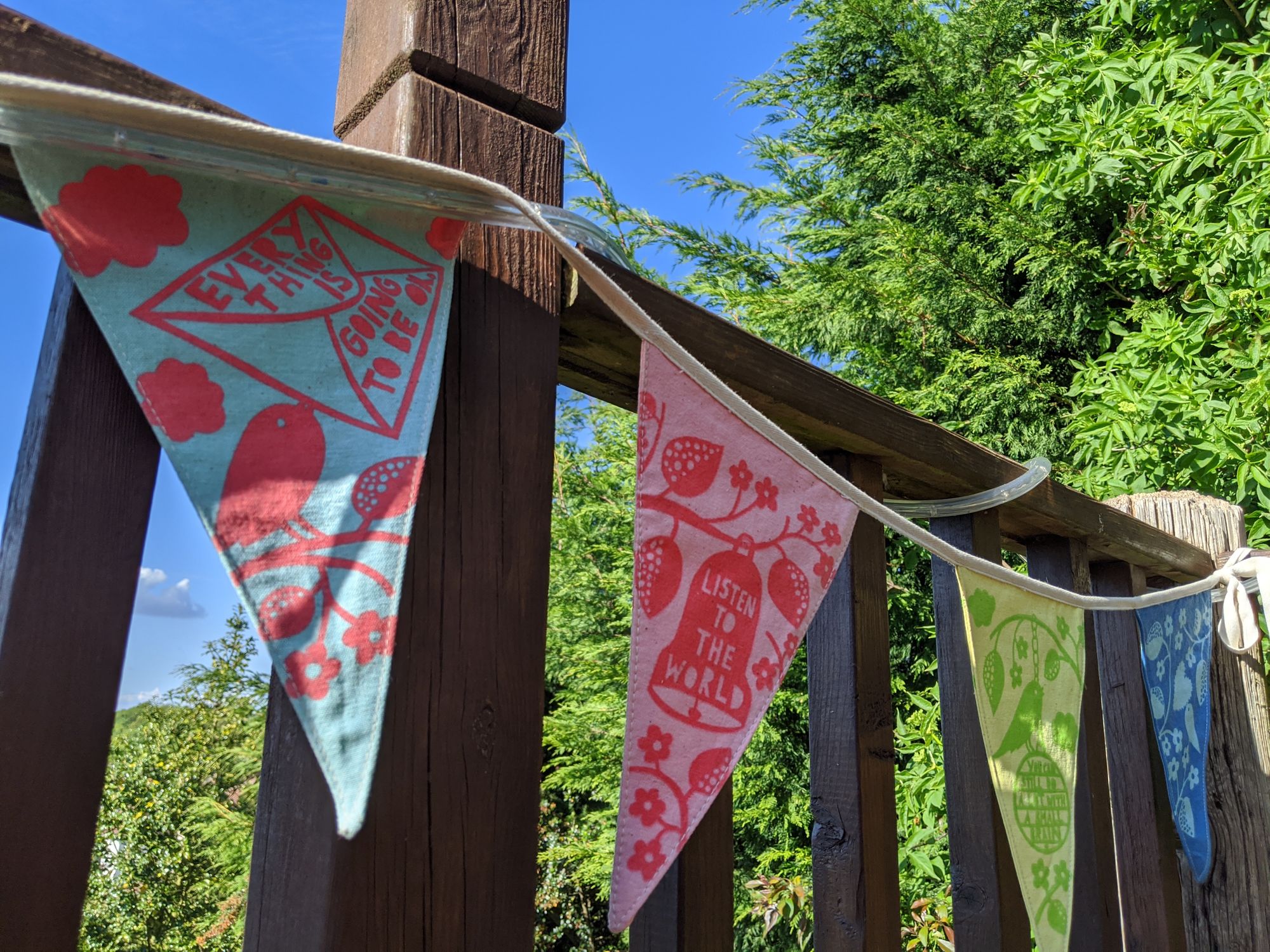 Photo of brightly coloured bunting tied to a wooden fence. One pink and red flags has Listen to the World written on i