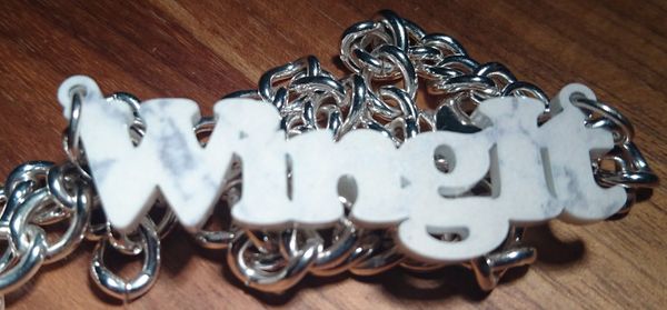 A necklace with a white/grey pendant saying 'WingIt' on a chunky silver chain