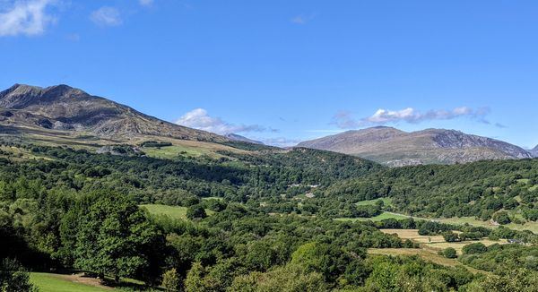 Green hills with luscious grass and trees.  Blue sky with a mountain in the distance