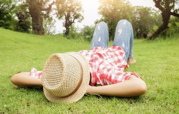 Person lying on their back looking at the sky, partly hidden with a hat on their head.